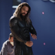 Aquaman (Jason Momoa) in his superhero suit has a stern look on his face while standing on a rocky beach in Lost Kingdom.